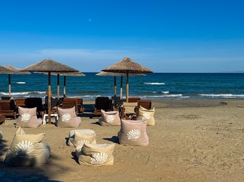 Παραλία Malabar στην Αρτέμιδα με ξύλινες ξαπλώστρες, ψάθινες ομπρέλες και πουφ στην άμμο, δίπλα στα γαλάζια νερά, προσφέροντας χαλάρωση και δωρεάν ξαπλώστρες τις καθημερινές.